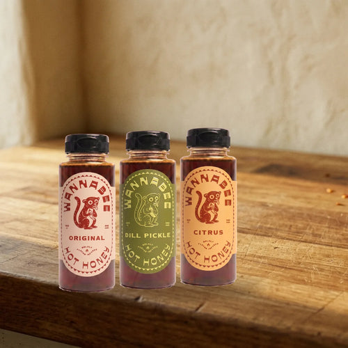 Three Wannabee hot honey bottles on a wooden counter: Original, Dill Pickle and Citrus.